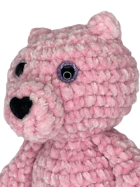 a pink crocheted teddy bear is shown against a black background