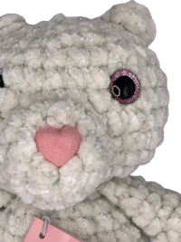 a white crocheted teddy bear with a pink tag